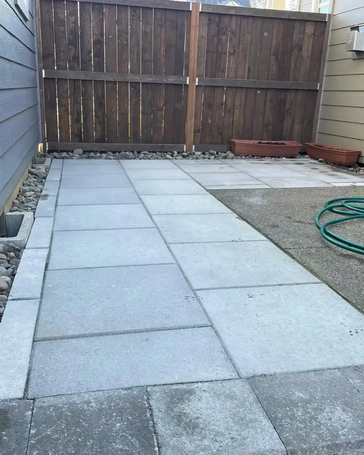 Concrete paver patio with river rock border installed in a compact fenced backyard by HD Landscape in Portland