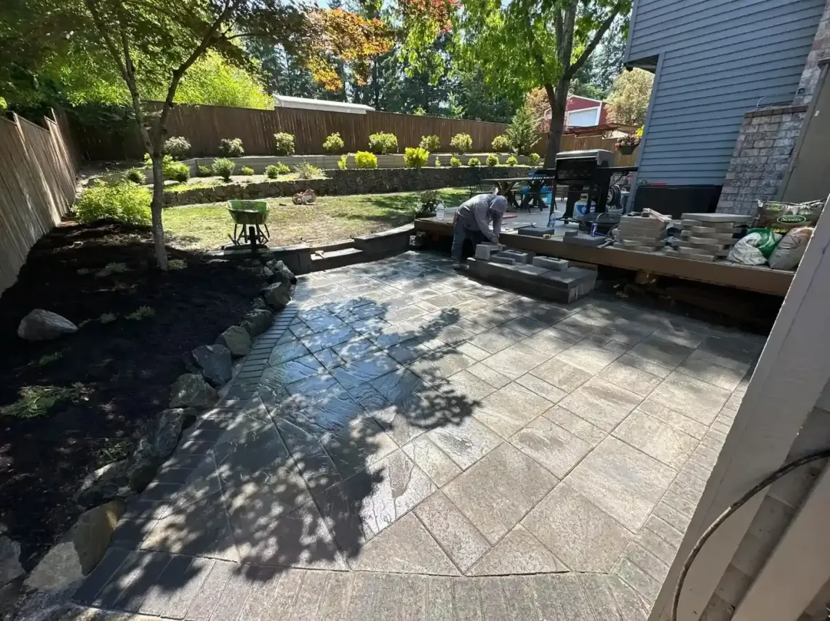 HD Landscape crew installing paver patio steps beside a boulder-edged mulch bed with terraced retaining wall in West Linn