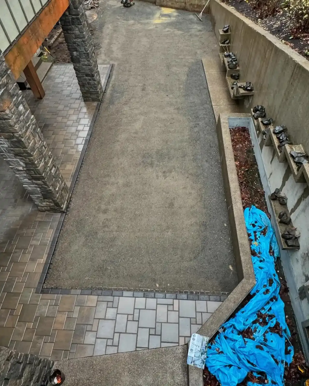 Overhead view of paver patio base prep with stone veneer wall, concrete retaining wall, and drainage channel by HD Landscape in Portland