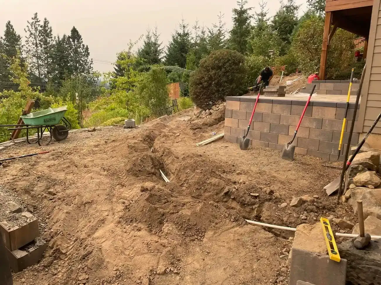 HD Landscape crew excavating drainage trenches alongside a block retaining wall on a hillside backyard in Wilsonville