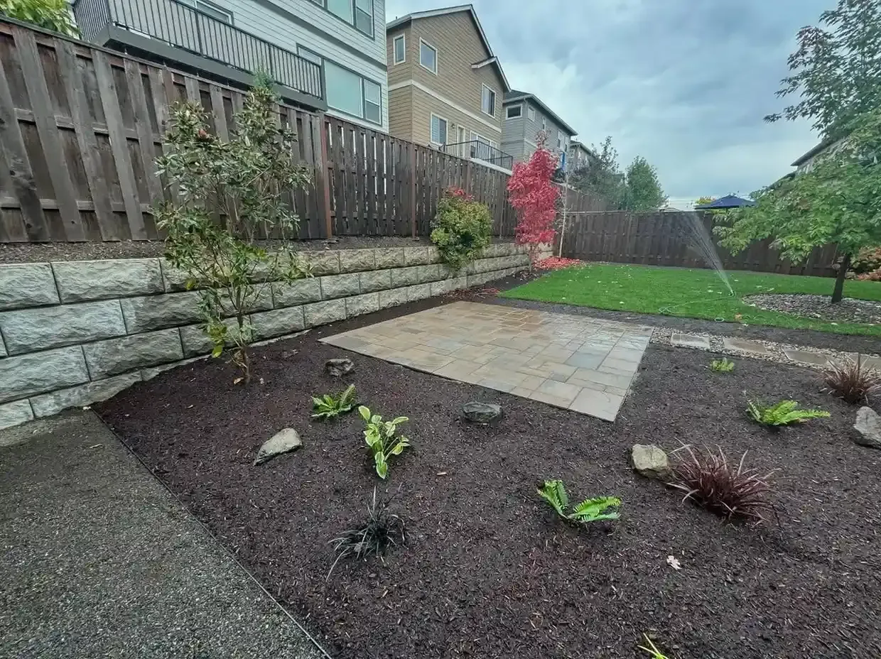 New backyard paver patio with block retaining wall, fresh mulch beds, and sprinkler-fed lawn by HD Landscape in Hillsboro