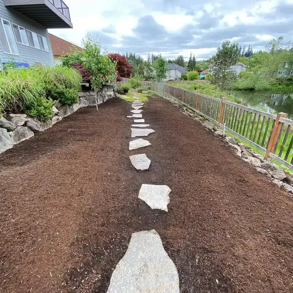 Natural stepping stone path through fresh mulch bed with boulder border along waterfront backyard by HD Landscape in Clackamas