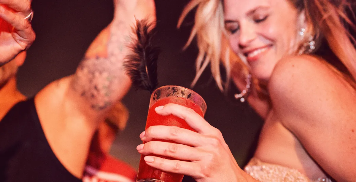Smiling woman dancing and holding a vibrant cocktail during an energetic themed party aboard the cruise.