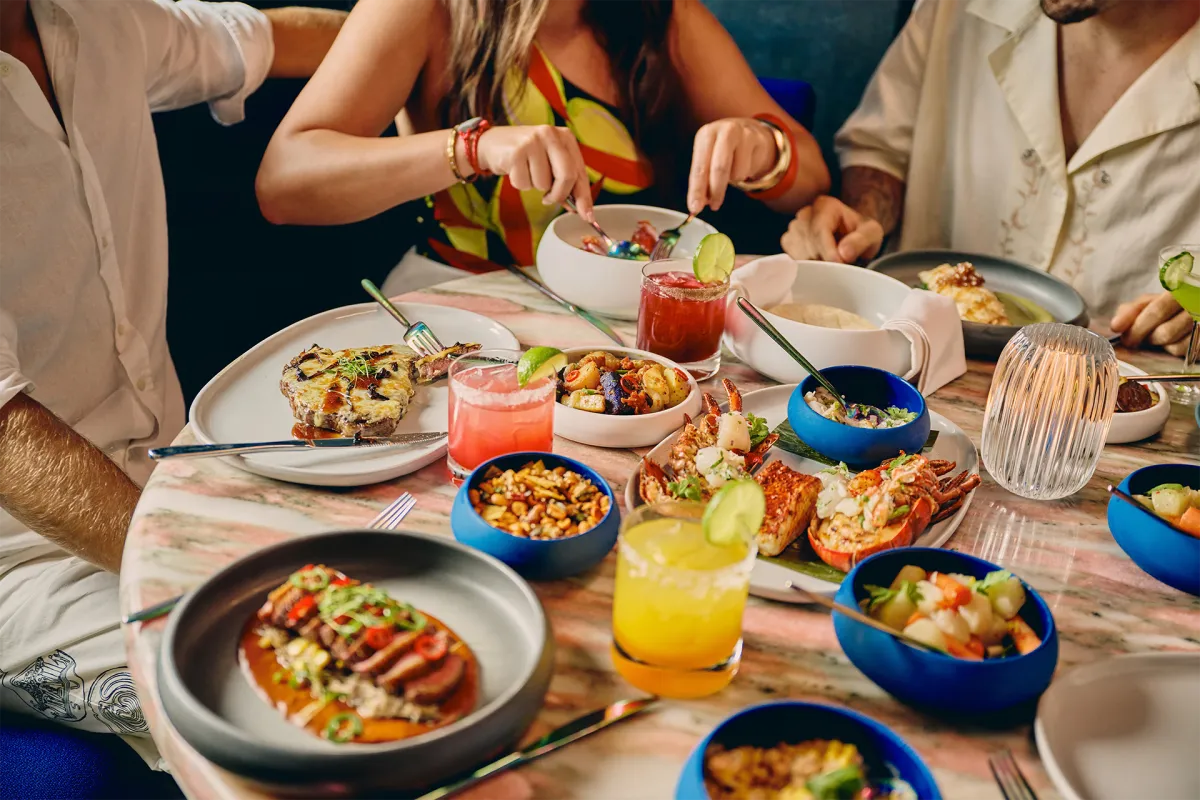Close-up of a table filled with gourmet dishes, cocktails, and small plates as guests enjoy a Michelin-star dining experience aboard the cruise.