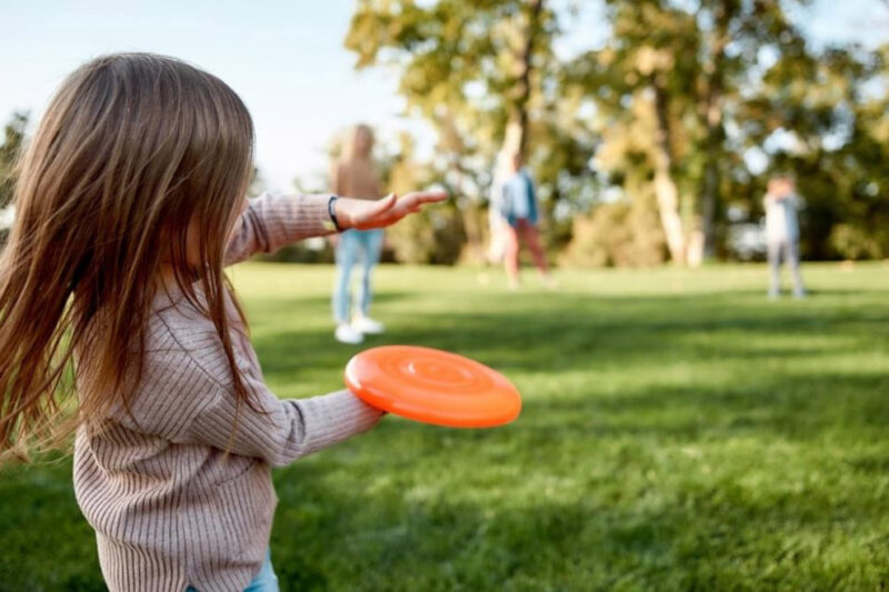 Girl throwing a frisbee on a open green lawn in a community park