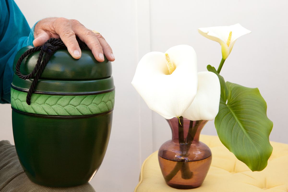 Person holding a green cremation urn next to white memorial flowers