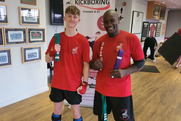 Two Senshi kickboxing adults smiling with their new belts after a successful grading.
