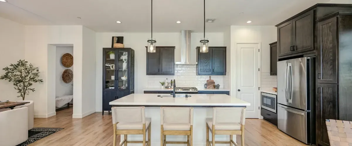 Modern dark wood kitchen with large island, pendant lights, and stainless steel appliances.
