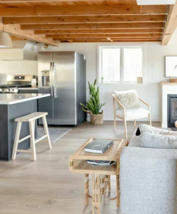 A warm, bright open-plan kitchen and living room featuring wooden beams, a kitchen island, and a cozy armchair.