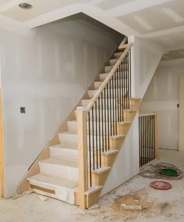 A new light wood staircase with black balusters and covered treads under construction in a house.