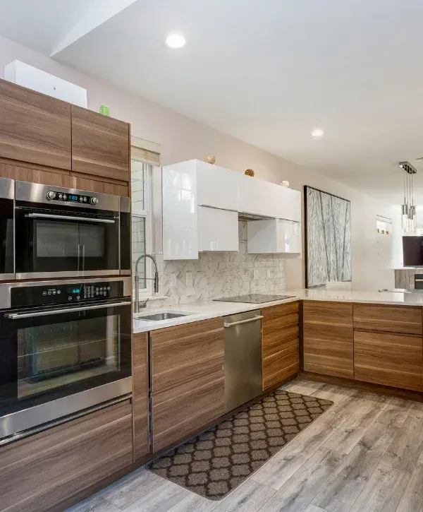 A modern kitchen featuring wood base cabinets, white upper cabinets, stainless steel appliances, and a marble tile backsplash.