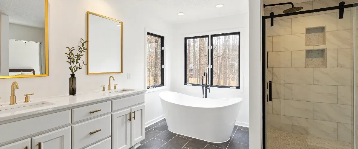 A luxurious white bathroom featuring a freestanding tub, double vanity with gold fixtures, and a glass-enclosed shower.