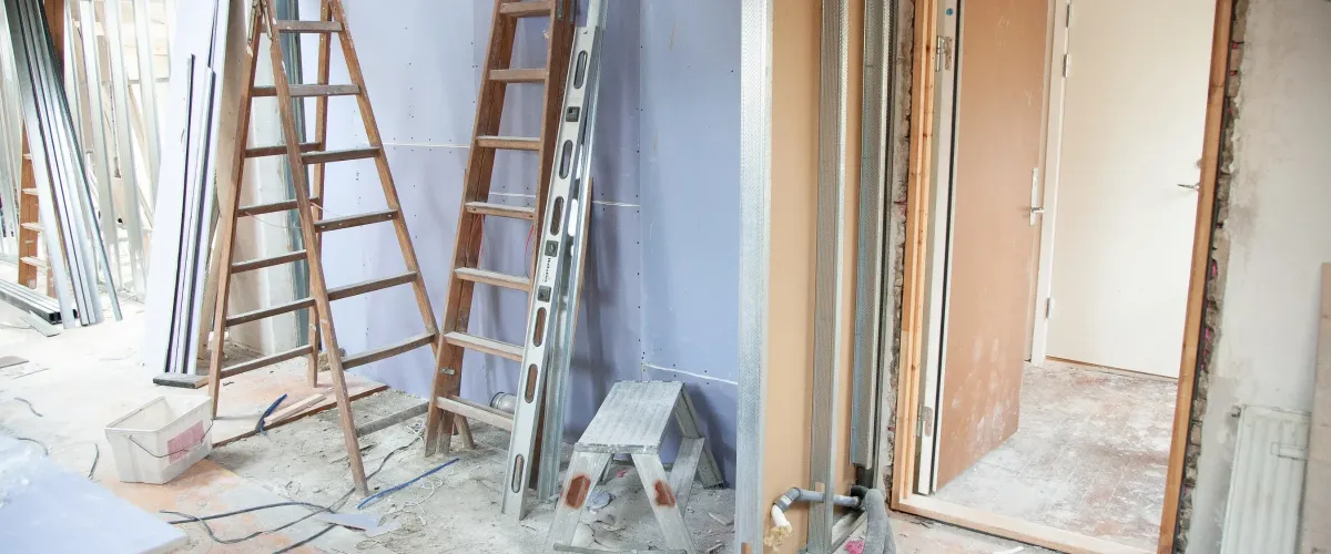 An interior construction site with wooden ladders, metal studs, drywall, and a partially installed doorframe.
