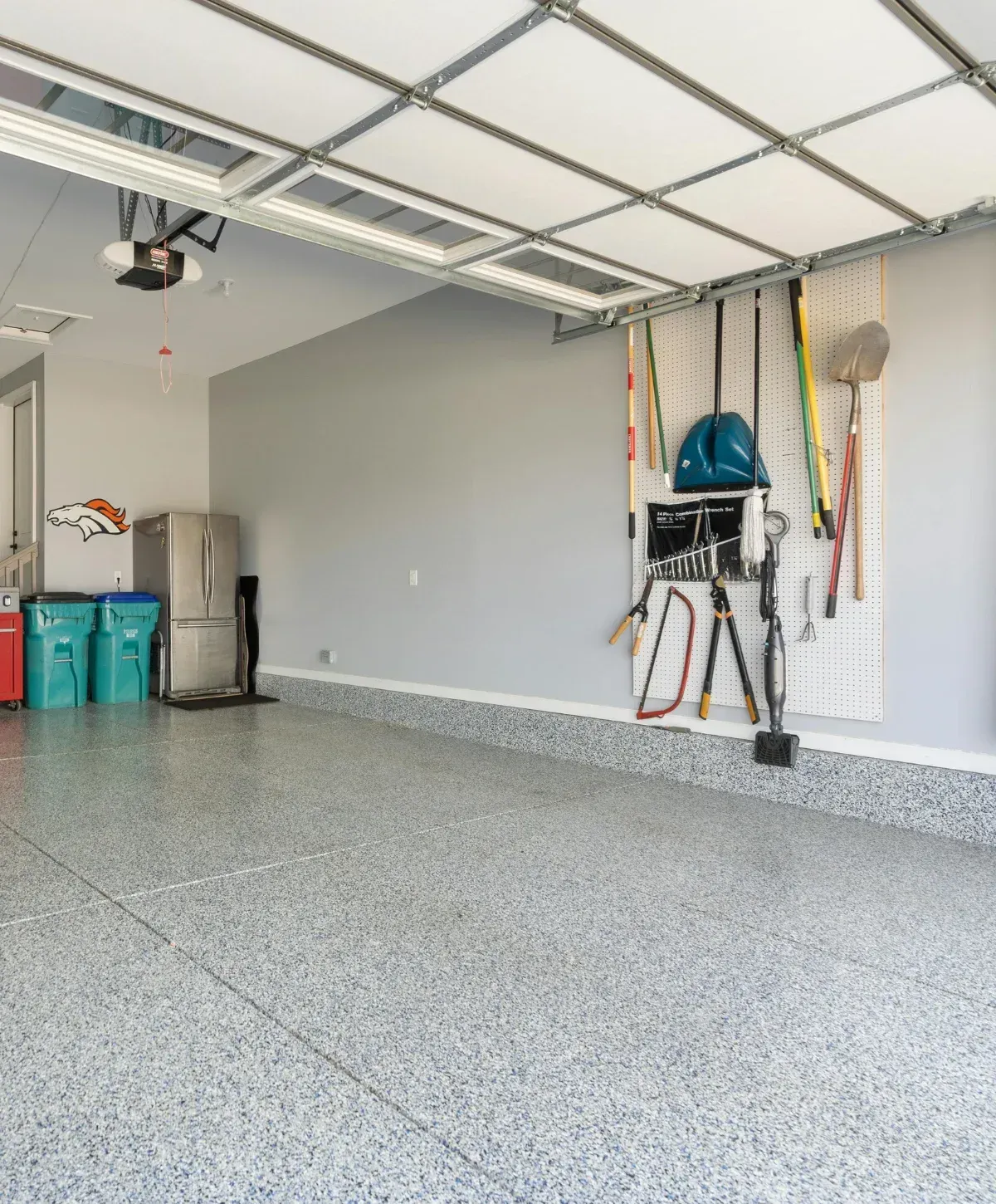 A clean, organized garage with light grey walls, a speckled blue epoxy floor, and gardening tools hanging on a pegboard.