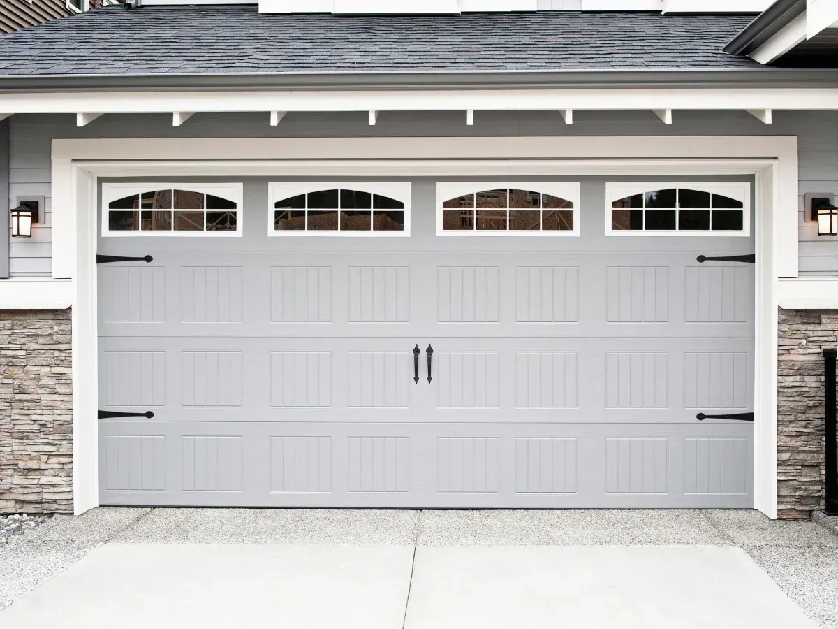 A full view of a modern gray garage door with decorative windows and black hardware on a house with stone accents.