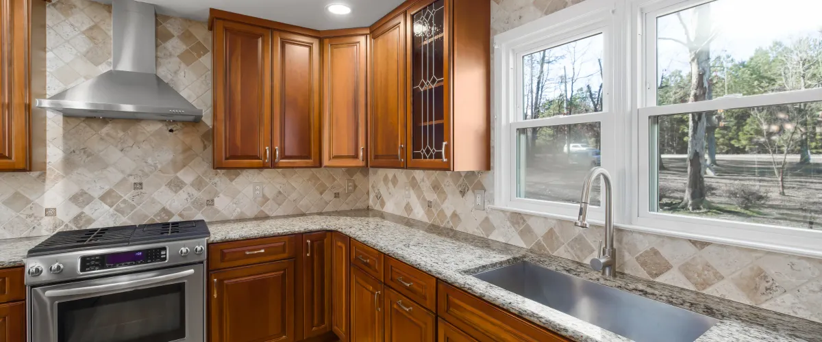 A clean kitchen corner with cherry wood cabinets, granite countertops, a diamond-patterned tile backsplash, and a large window.