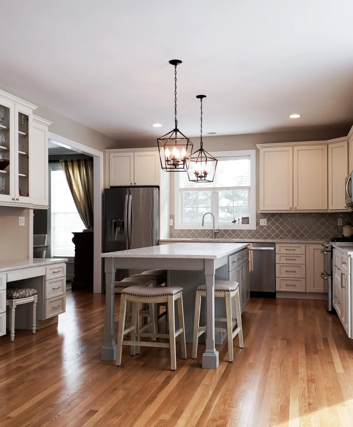 A modern kitchen with light wood floors, white cabinets, a gray island with stools, and stainless steel appliances.
