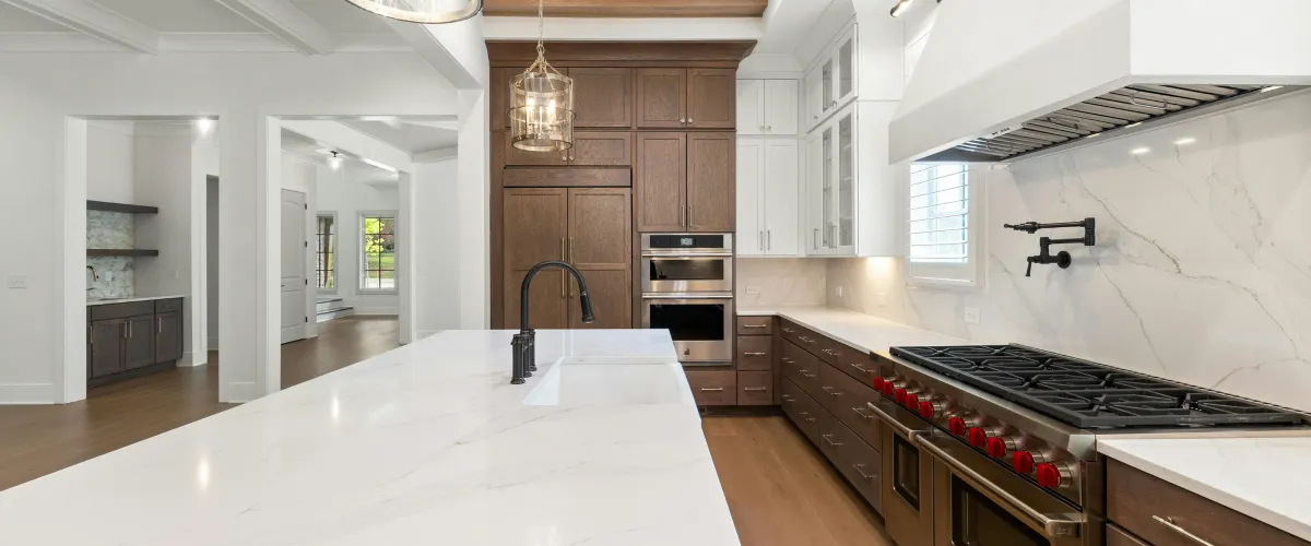 A luxurious kitchen featuring a large white marble island with a black faucet and a professional range with red knobs.