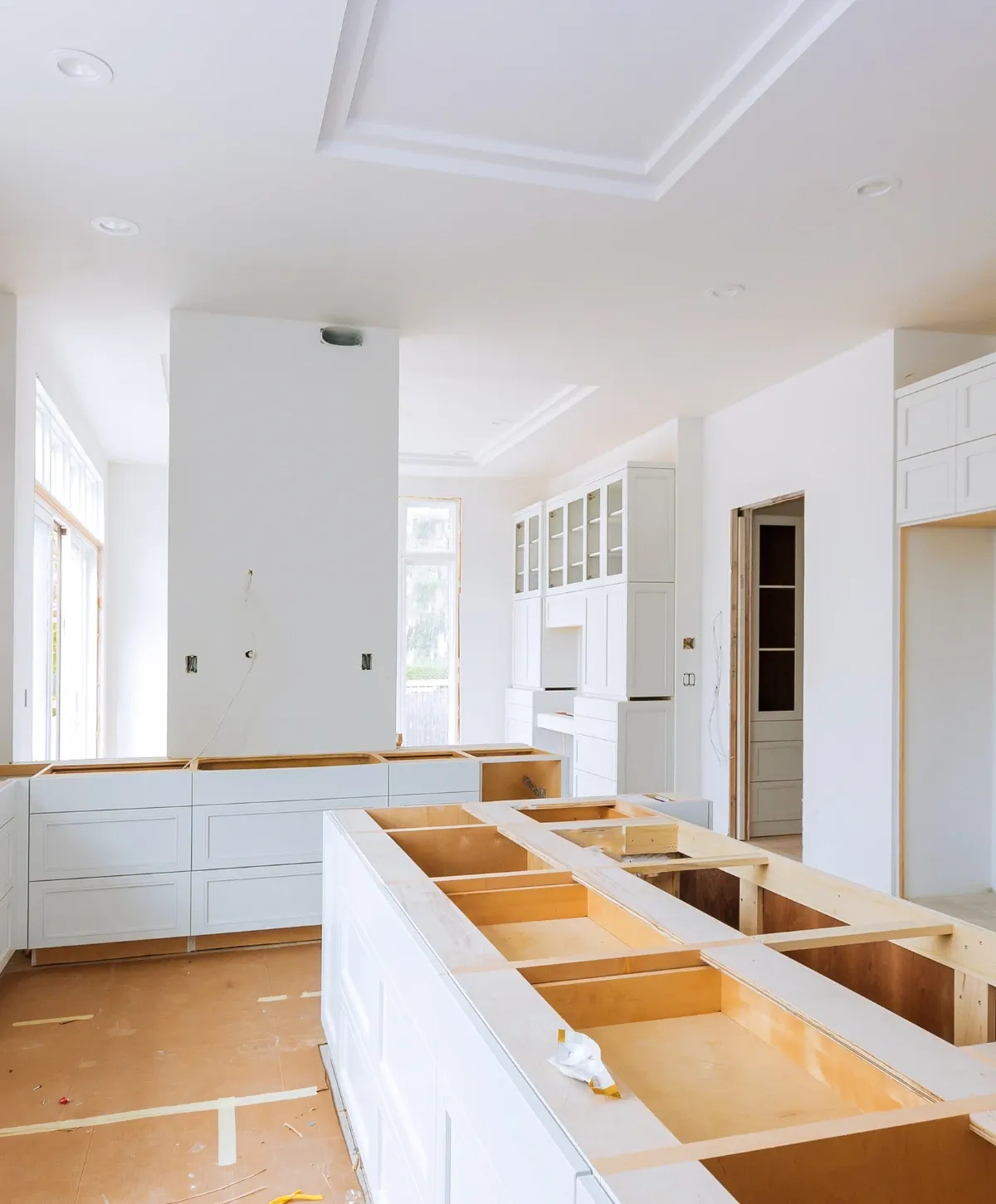 A kitchen under construction with dark wood upper and lower cabinets installed, exposed outlets, and a large window.