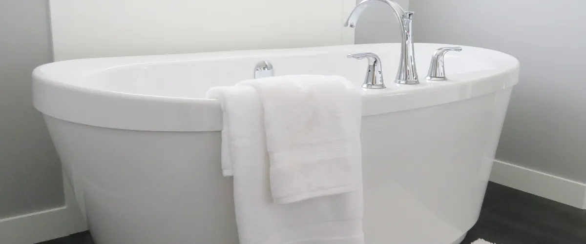 A modern white freestanding bathtub with chrome fixtures and a folded white towel draped over its edge.