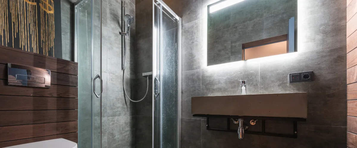 A clean, well-lit A sleek modern bathroom featuring dark gray tiled walls, a glass shower enclosure, a concrete sink with a backlit mirror, and dark wooden paneling.interior with a closed white sectional door, gray epoxy floor, and empty wall shelves.