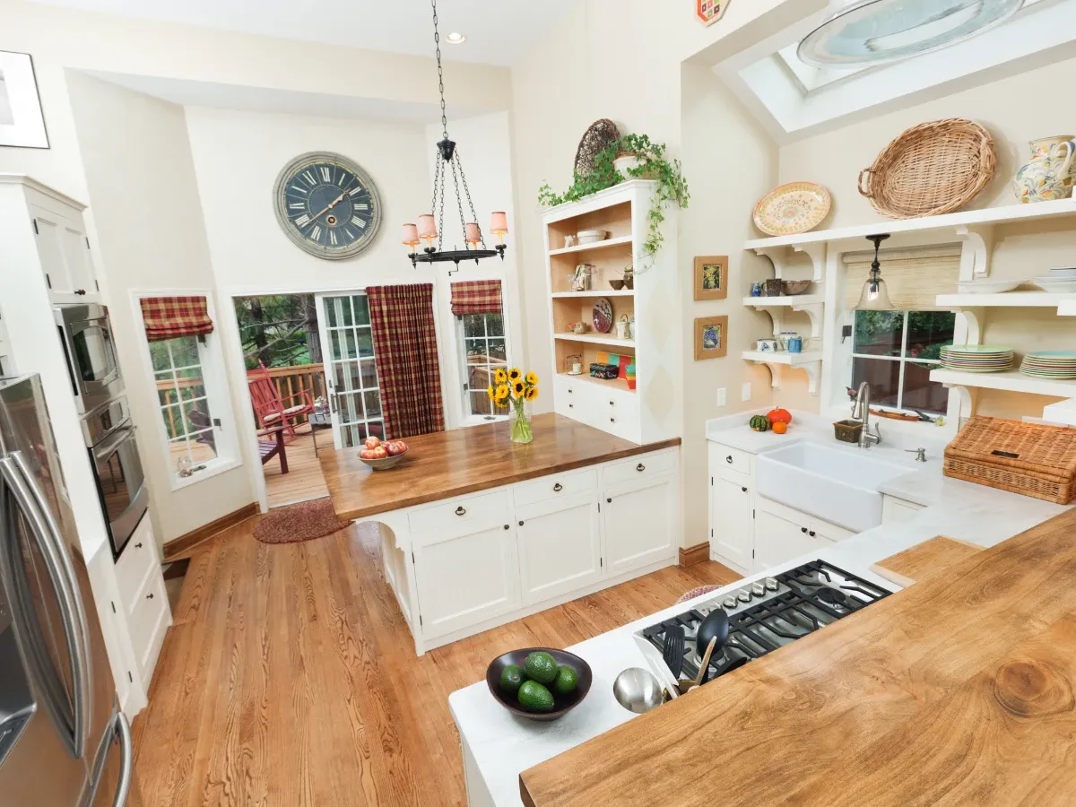 A bright, spacious farmhouse-style kitchen featuring a large wooden island, white cabinets, stainless appliances, and a view to a deck.