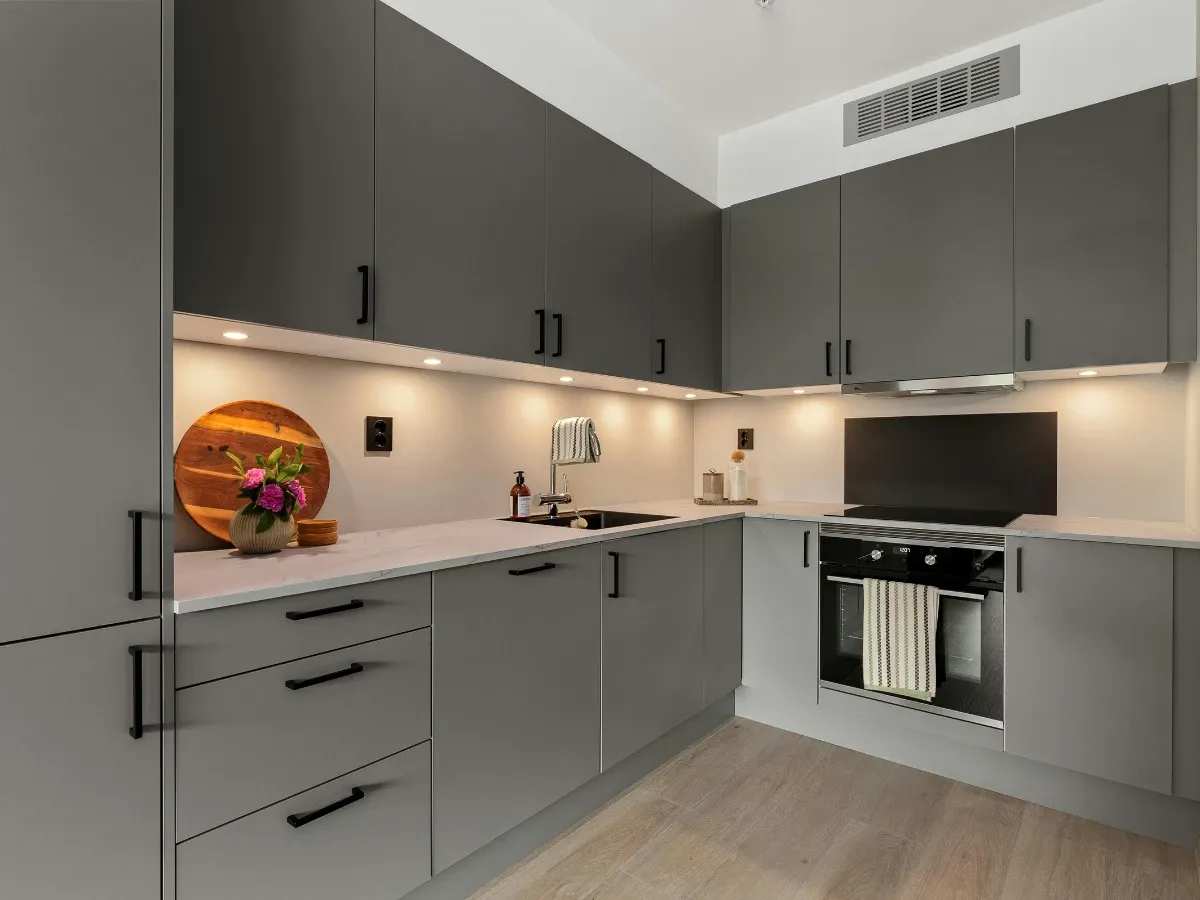 A modern kitchen featuring sleek grey cabinets, light marble countertops, integrated appliances, and warm under-cabinet lighting.