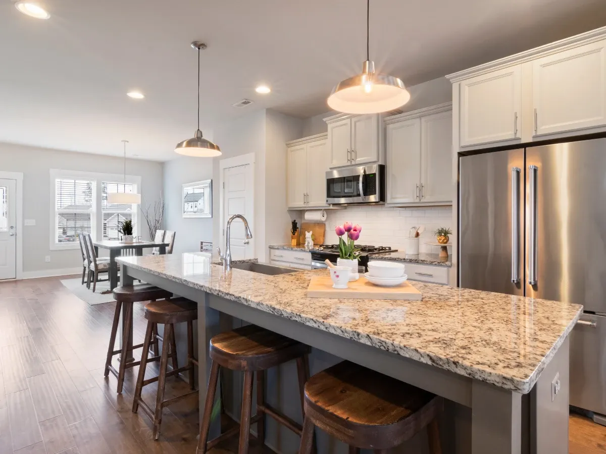 A modern open-concept kitchen with a large granite island and wooden stools, extending into a dining area with a table and chairs.