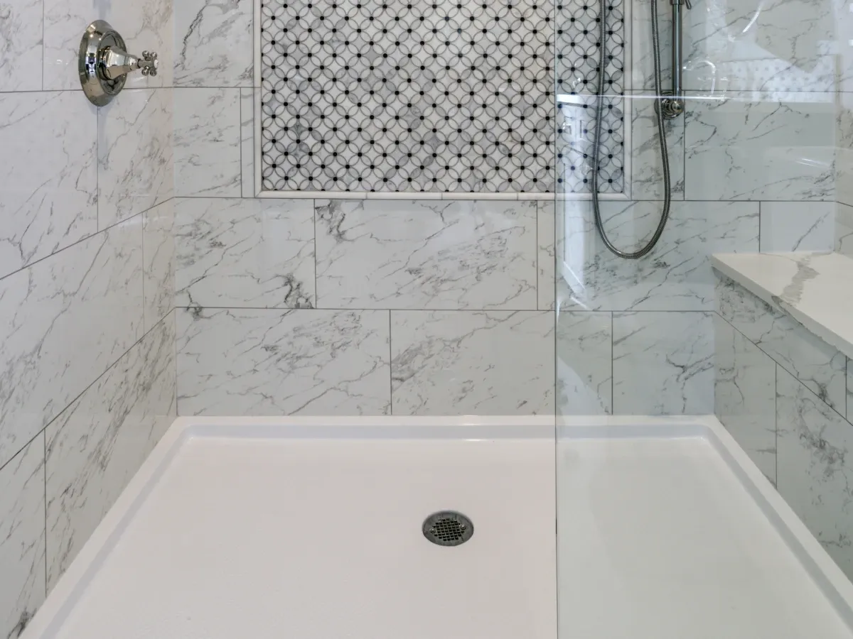 A clean, modern walk-in shower with white marble-look subway tiles, a mosaic accent, a white base, and a glass partition.