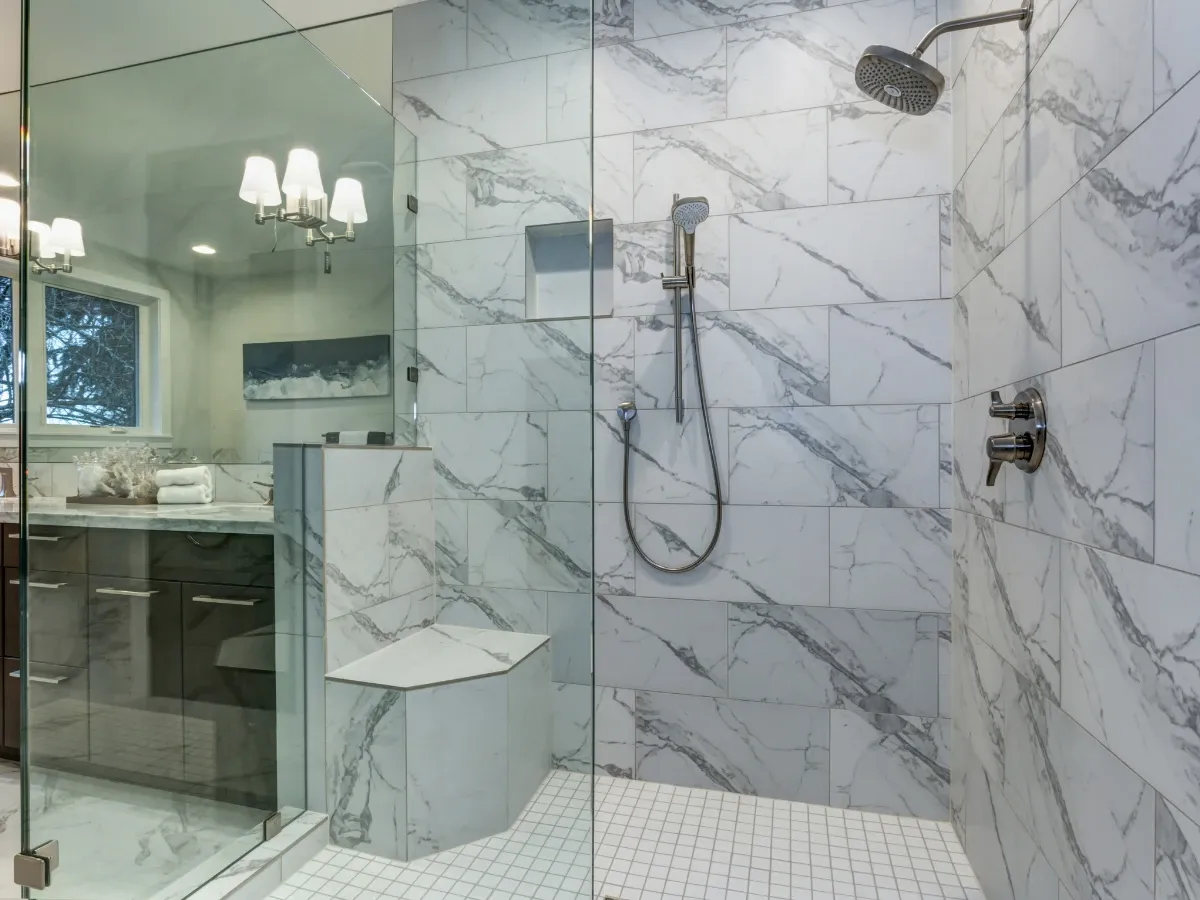 A luxurious walk-in shower with white and gray marble-patterned tiles, glass enclosure, and a built-in bench.