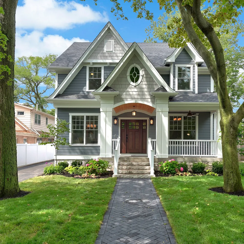 Beautiful, newly renovated two-story home with gray siding, white trim, a covered front porch, and a manicured lawn with a stone walkway, surrounded by mature trees in a suburban neighborhood.