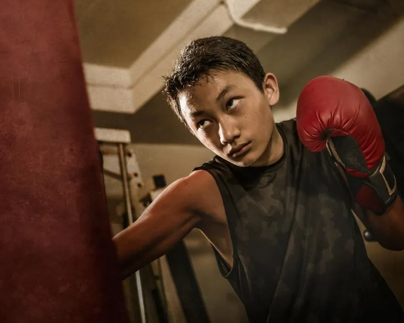 Smiling young woman holding large red boxing gloves up near her face, looking directly at the camera.