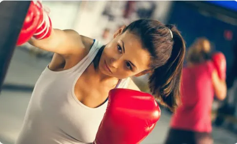 Smiling young woman holding large red boxing gloves up near her face, looking directly at the camera.