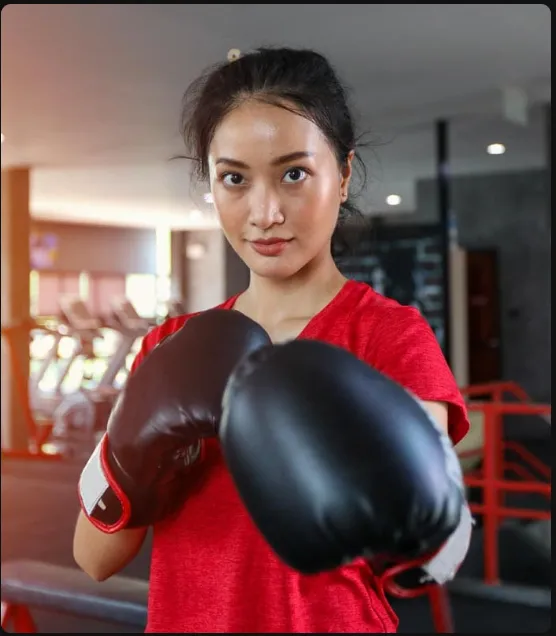 Smiling young woman holding large red boxing gloves up near her face, looking directly at the camera.