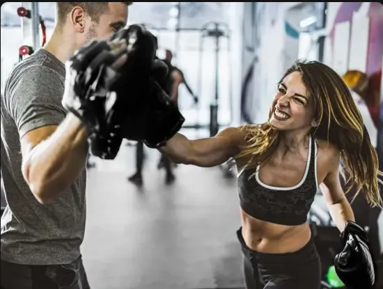 Smiling young woman holding large red boxing gloves up near her face, looking directly at the camera.