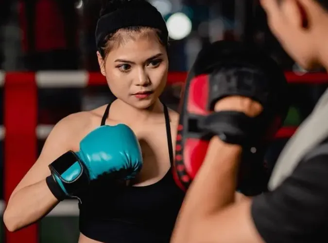 Smiling young woman holding large red boxing gloves up near her face, looking directly at the camera.