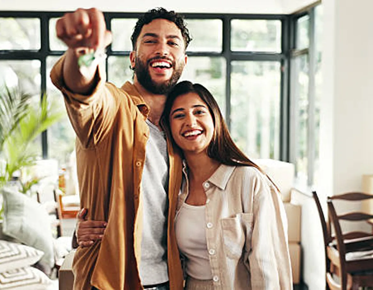 Happy couple holding house keys in front of their new home, smiling after mortgage approval