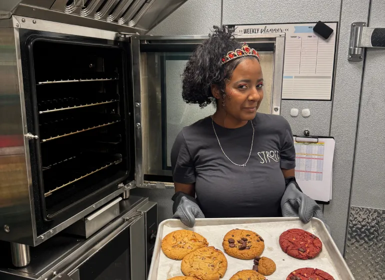 Stroll Cafe team member holding a tray of freshly baked cookies in front of a commercial oven, highlighting hands-on food preparation and dynamic daily roles.
