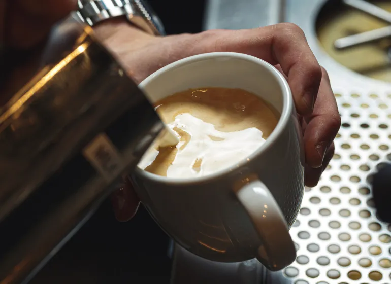 Close-up of a barista expertly steaming milk and pouring latte art, representing the specialty coffee and espresso training provided at Stroll Cafe.