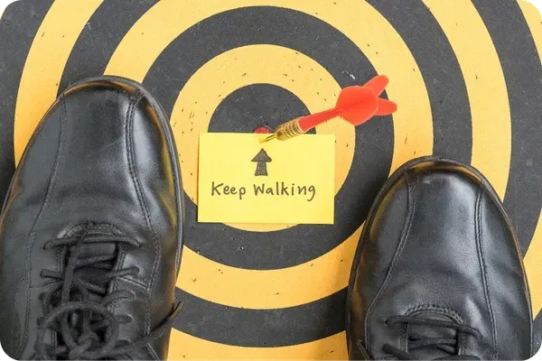 Zapatos frente a un blanco con una nota que dice Keep Walking simbolizando avanzar con decisiones conscientes hacia el objetivo