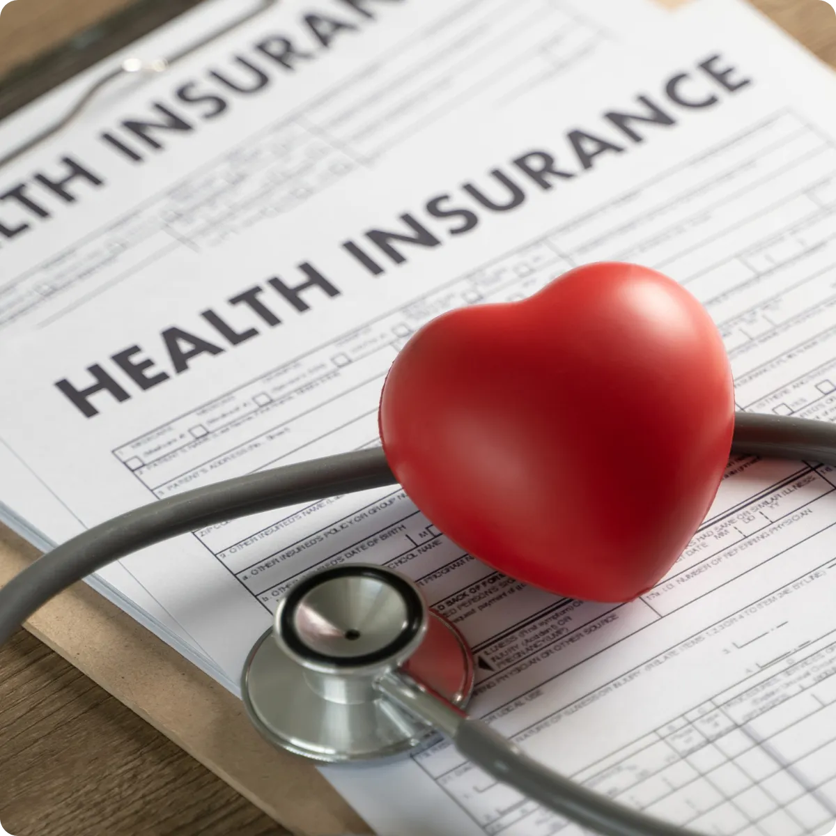 Health insurance forms and red heart stress ball on clipboard
