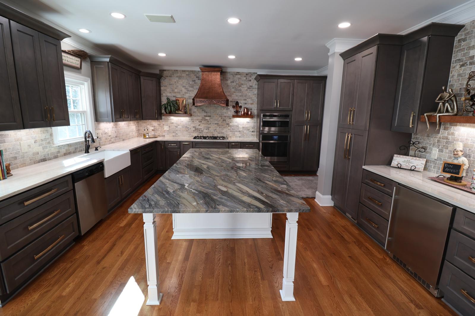 A female designer and a couple review kitchen plans at a sunlit table, samples of cabinetry and countertops spread out, 1:1 aspect ratio.