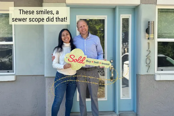 Happy home buyers Yury and Will holding a 'Sold' key in front of their new Tampa Bay home — sewer scope inspection saved them $36,000 in negotiated savings with Realtor Laura Marie