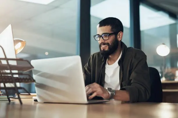Smiling SEO expert with glasses managing a client CRM on his laptop