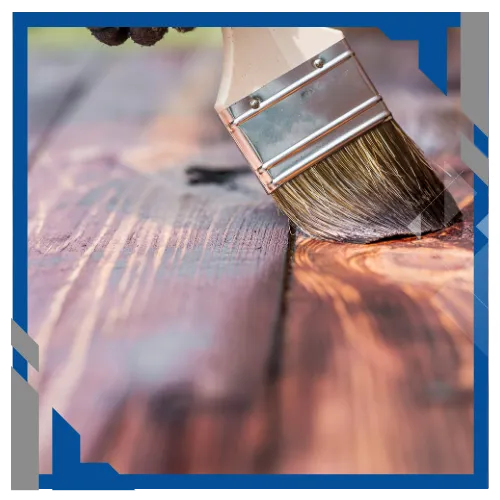 Paint brush applying coating to wood surface for deck or fence painting.