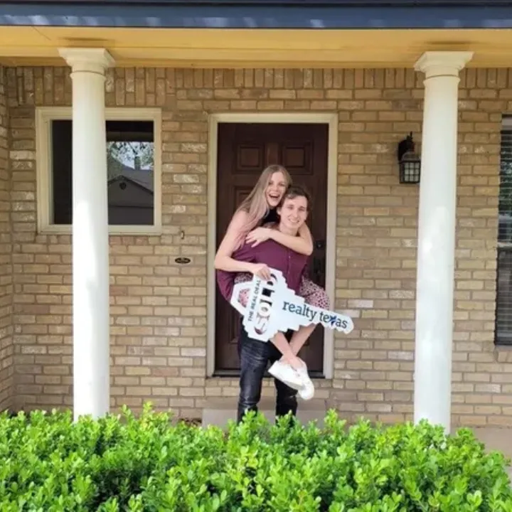 Excited new homeowners celebrating their purchase in Round Rock, TX, holding a Realty Texas key.