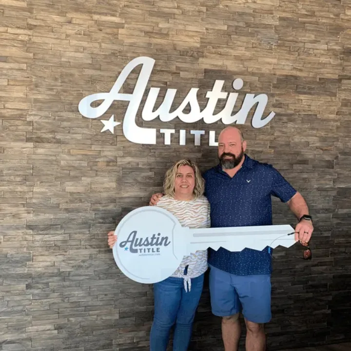 Happy homebuyers celebrating their successful closing at Austin Title with a giant key.