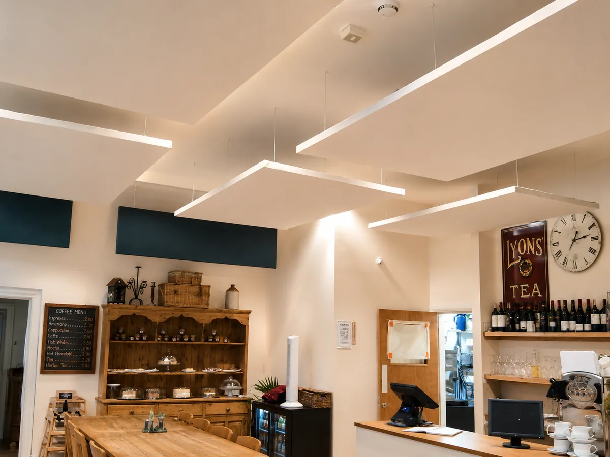 White suspended ceiling panels and dark wall panels above a café counter and furnishings.