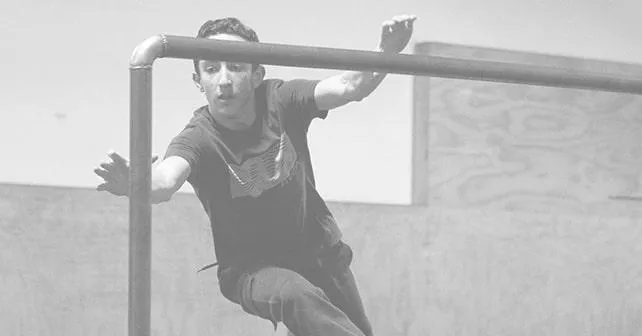A parkour student is mid-air, aiming to catch a bar and pull themselves closer to the camera.