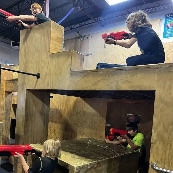 Four kids with various Nerf guns are taking aim from various positions